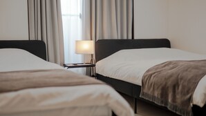 Una camera d'albergo con due letti singoli, un comodino con lampada e una finestra con tende.