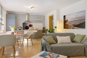 A modern living room with a grey sofa, a dining table, and a kitchen in the background. - Apartment "Kornblume" with Private Terrace and Wi-Fi (Bodman-Ludwigshafen)