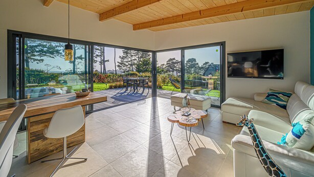 A modern living room with a wooden ceiling, large windows, a dining area, and a sofa. - Egret - La Laïta (Guidel)