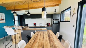 A modern kitchen with a wooden table, white chairs, and a hanging light fixture. - Egret - La Laïta (Guidel)