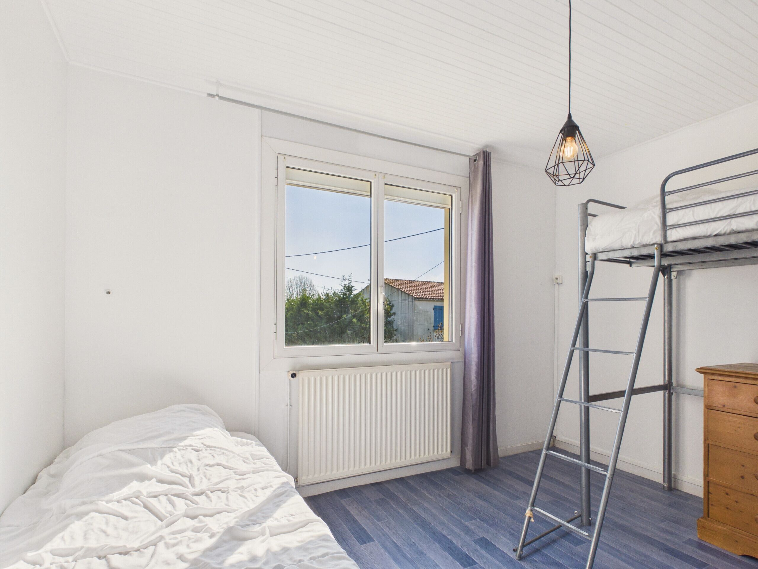 A bedroom with a bunk bed, a radiator, a window with curtains, and a wooden dresser.