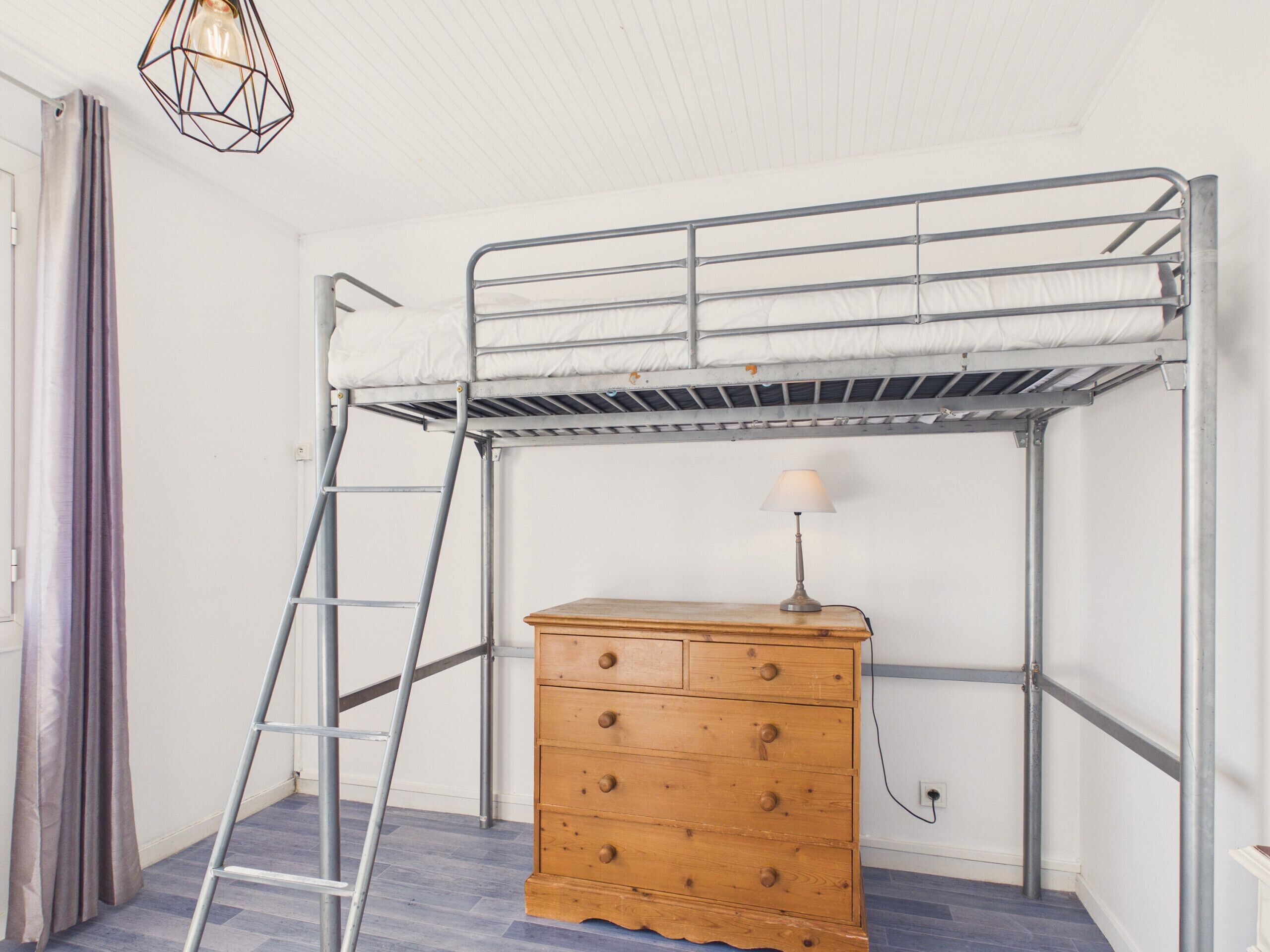 Ein Stockbett mit einer Leiter, eine Holzkommode und eine Lampe.