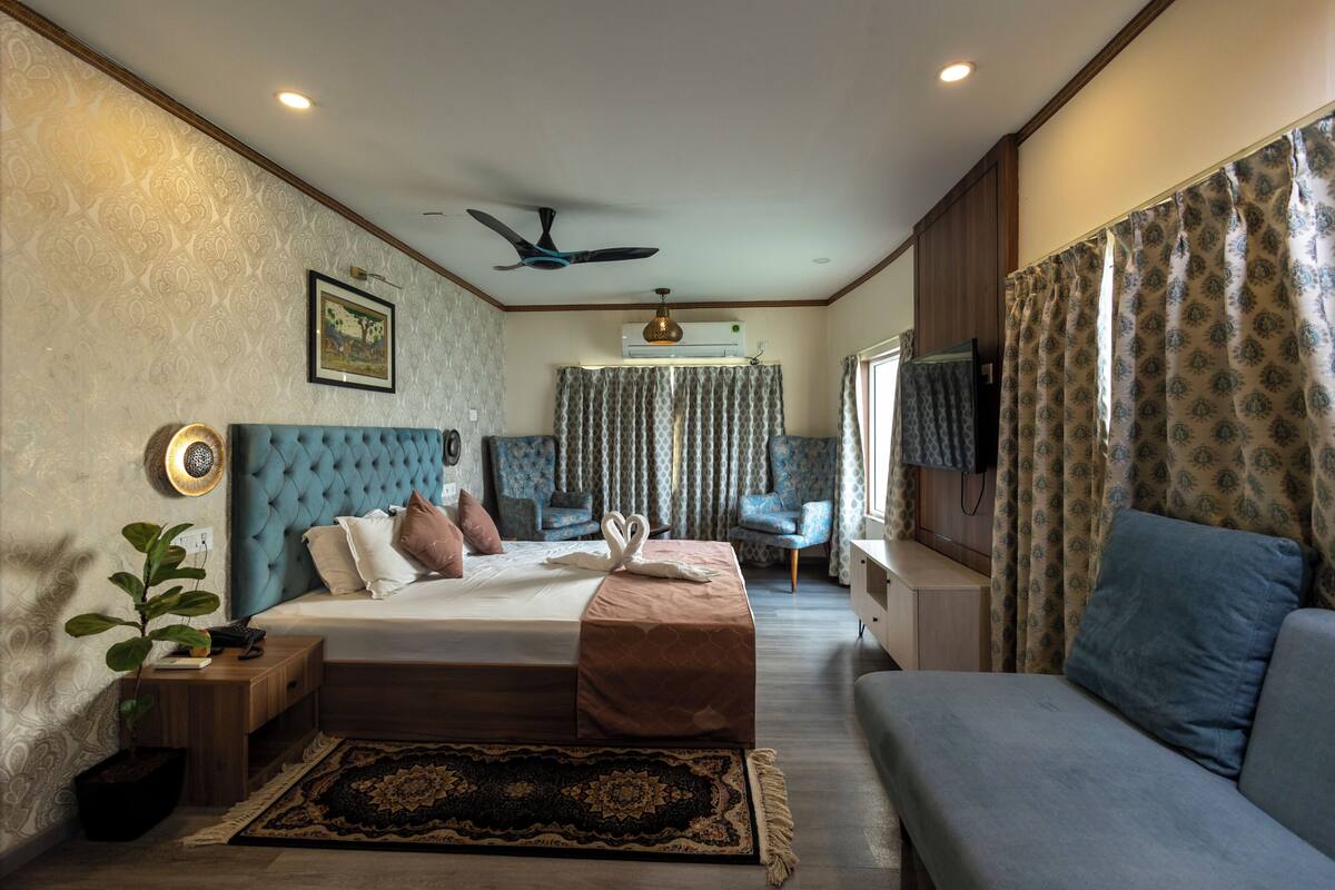 A bedroom with a bed, a sofa, a TV, a ceiling fan, and a window with curtains.