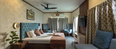 A bedroom with a bed, a sofa, a TV, a ceiling fan, and a window with curtains.