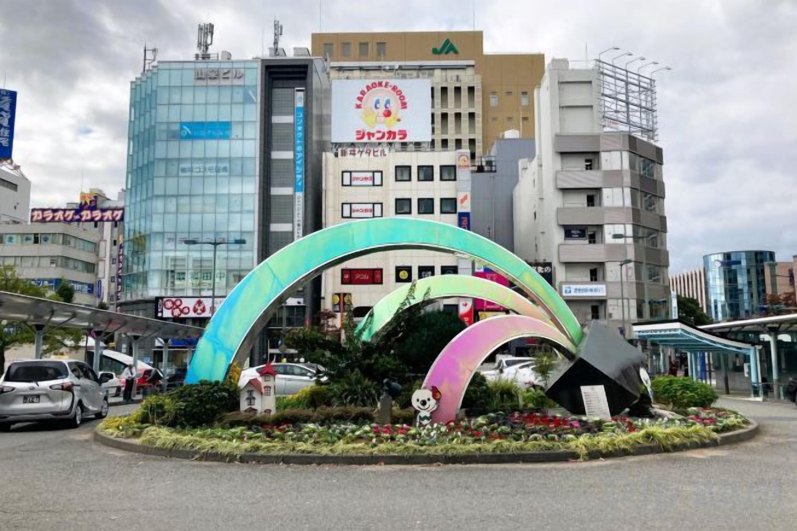 A roundabout with colorful arches and a panda statue, surrounded by buildings and cars.