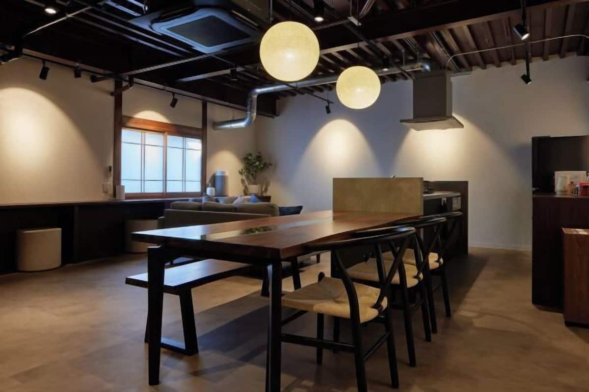 Een modern interieur met een lange eettafel, stoelen, hanglampen, een bank en een keukenhoek.
