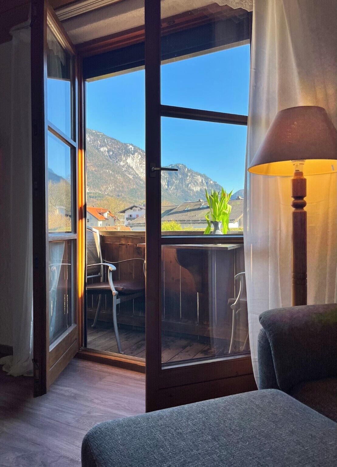 Een kamer met een groot raam, een stoel, een tafel en een lamp.
