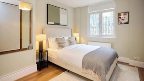 A bedroom with a bed, bedside table, lamp, mirror, window, and artwork. - The Tufnell Threshold (London)