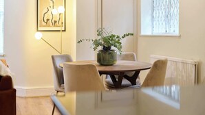 A dining area with a round table, chairs, a potted plant, a framed artwork, and a window with blinds. - The Tufnell Threshold (London)