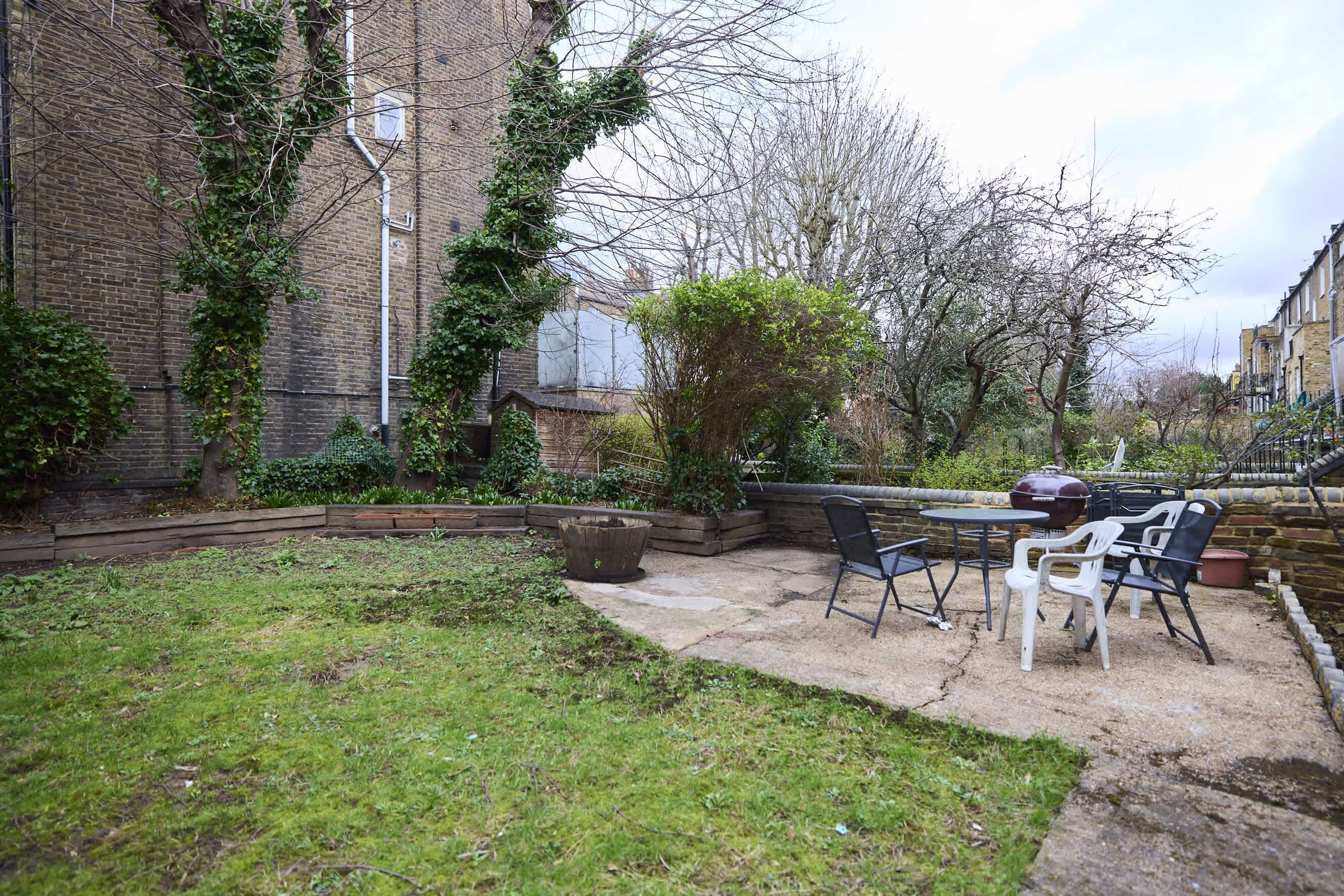 Un jardin avec une terrasse, des meubles d’extérieur et un mur en briques.