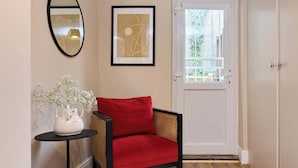 A room with a door, a framed abstract painting, a vase with flowers, and a red chair. - The Tufnell Threshold (London)