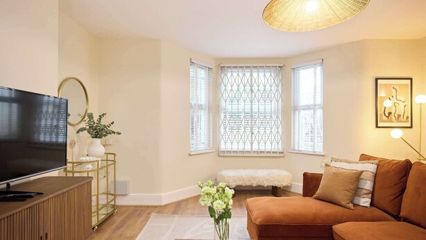 A living room with a flat-screen TV, a brown sofa, a glass coffee table, and a decorative vase with flowers. - The Tufnell Threshold (London)
