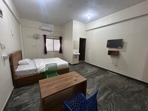 A hotel room with a bed, a desk, a chair, a TV, and a window with curtains. - Hotel O Jodi Sri Muneshwara Swamy Temple (Bengaluru)
