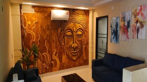 Un área de recepción con un mural de Buda, un sofá azul, una mesa de centro y una planta.