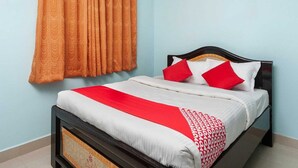 Una cama individual con cabecera, una colcha rojo y blanco, y almohadas rojas.