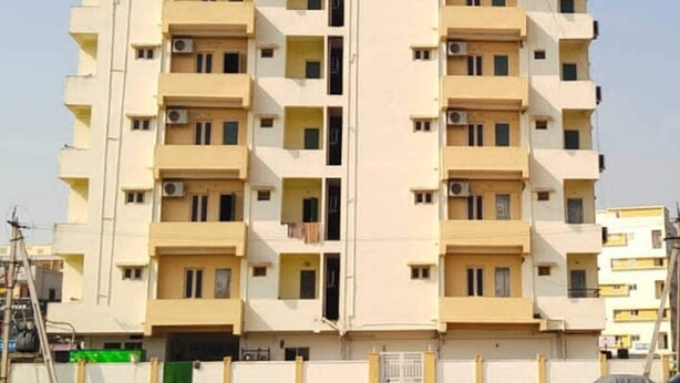 Un edificio residencial de varios pisos con balcones, unidades de aire acondicionado y una entrada con puerta de acceso.