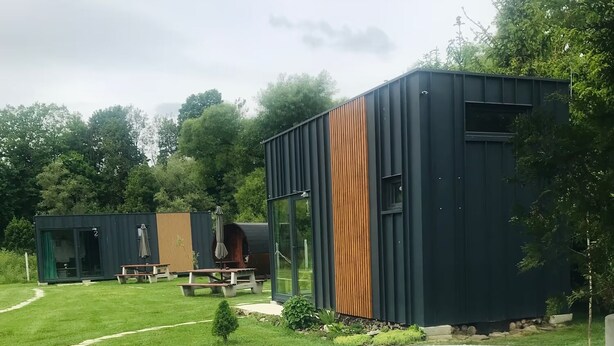 Een modern buitenzwembad met houten terras, picknicktafels en een heldere lucht.