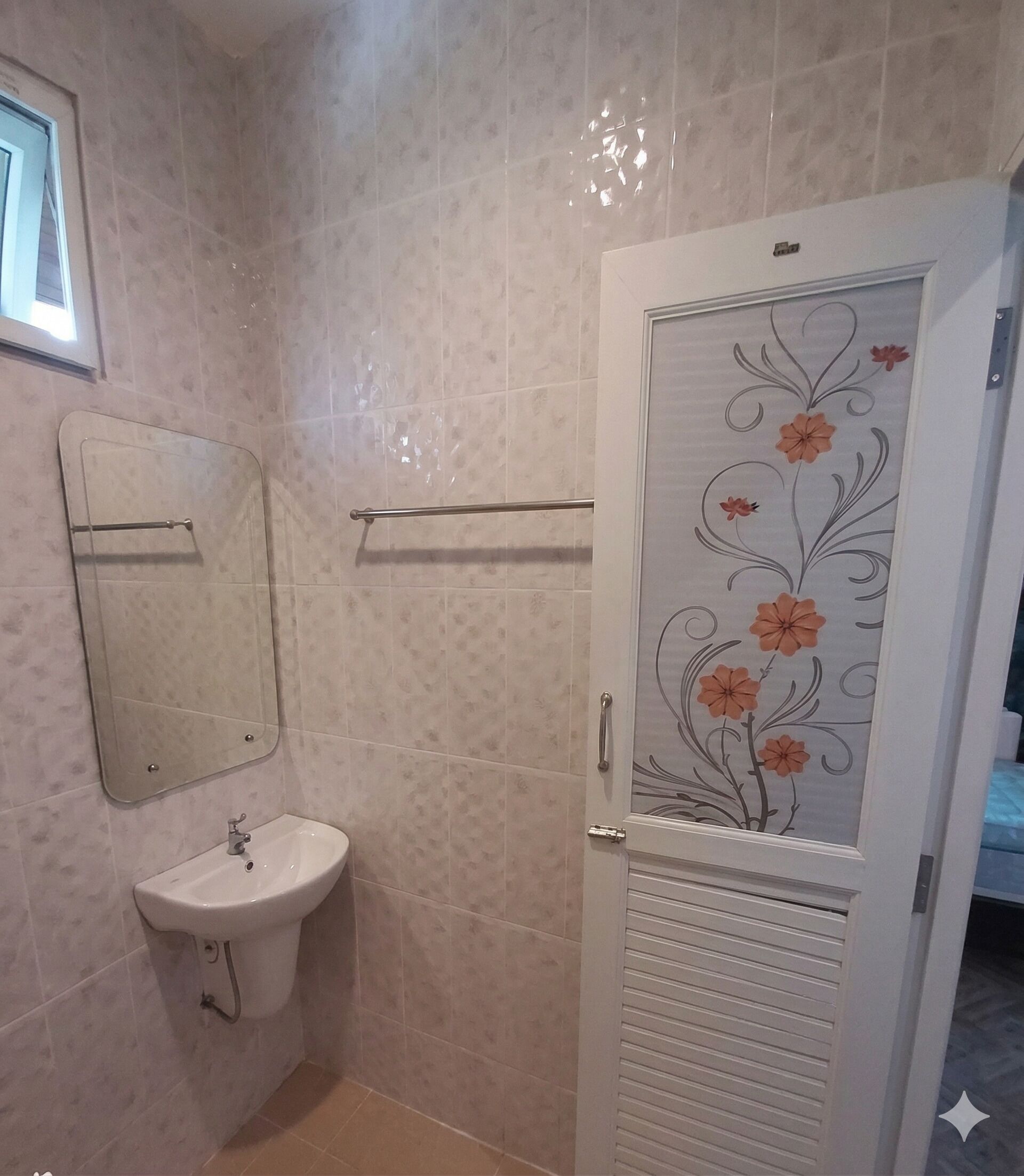 Um banheiro com pia, espelho, porta-toalhas e porta com padrão floral.