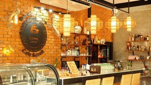 Una cafetería con pared de ladrillo, luces colgantes y una barra con sillas.