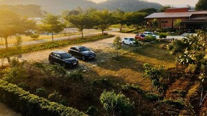 Un estacionamiento con varios coches, un edificio con techo rojo y un paisaje montañoso al fondo.