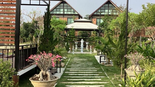 Un camino de jardín que lleva a un edificio con entrada cubierta y una estatua en el centro.