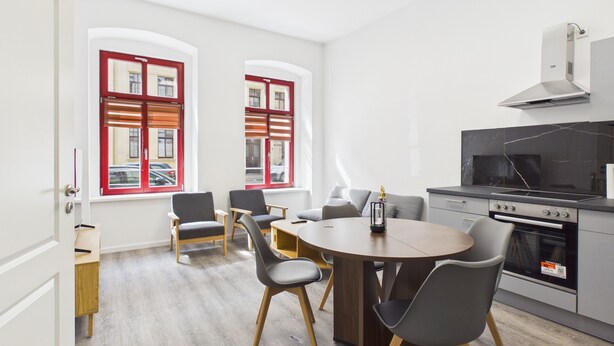 A modern kitchen with a built-in oven and stove, a dining table with chairs, and two windows with red frames. - Compact city apartment for 2 people (GÖ02) (Görlitz)