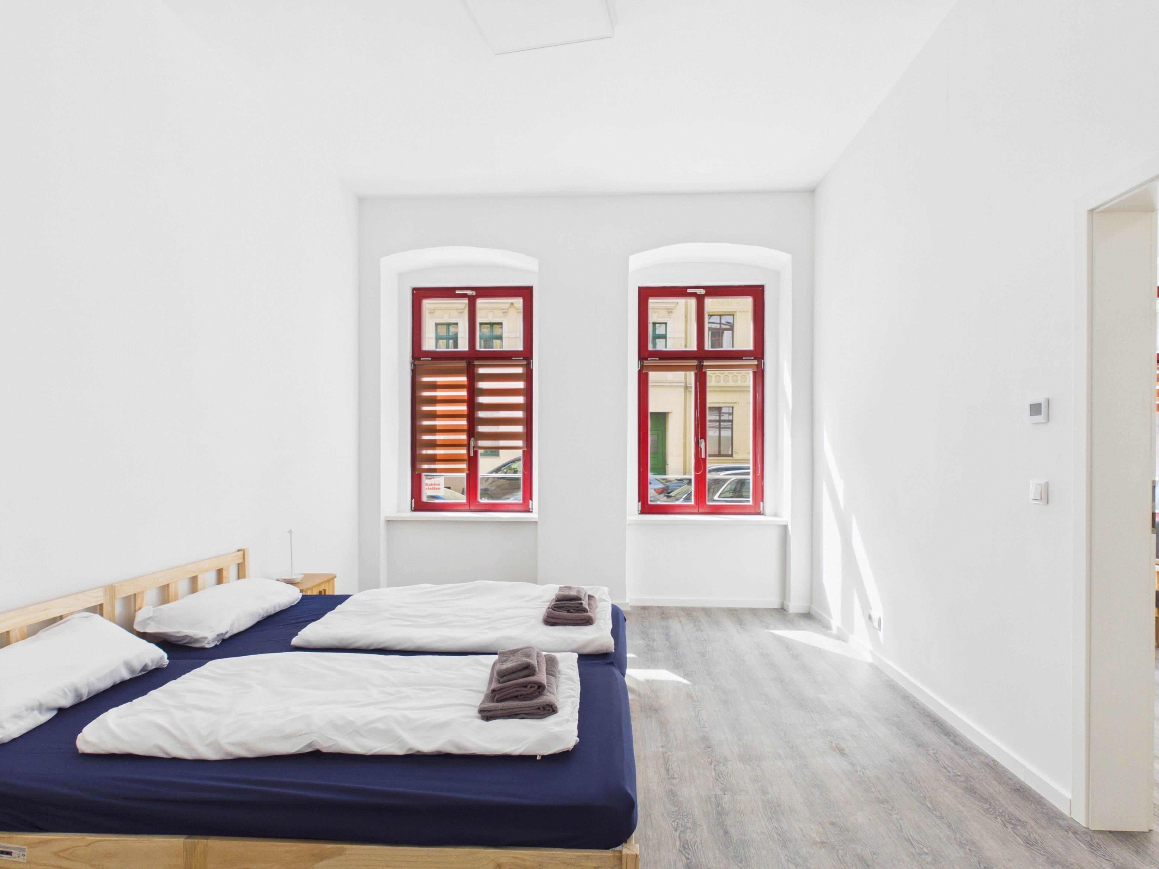 Ein Hotelzimmer mit zwei Betten, einem Holzkopfteil, einem Fenster mit roten Rollläden und einem hellen Boden.