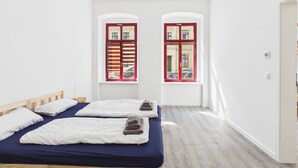 A hotel room with two beds, a wooden headboard, a window with red shutters, and a light-colored floor. - Compact city apartment for 2 people (GÖ02) (Görlitz)