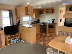 A compact kitchenette with a stove, sink, and a flat-screen TV. - Sundowner Holiday Park - Holiday Accommodation 15072 (Great Yarmouth)