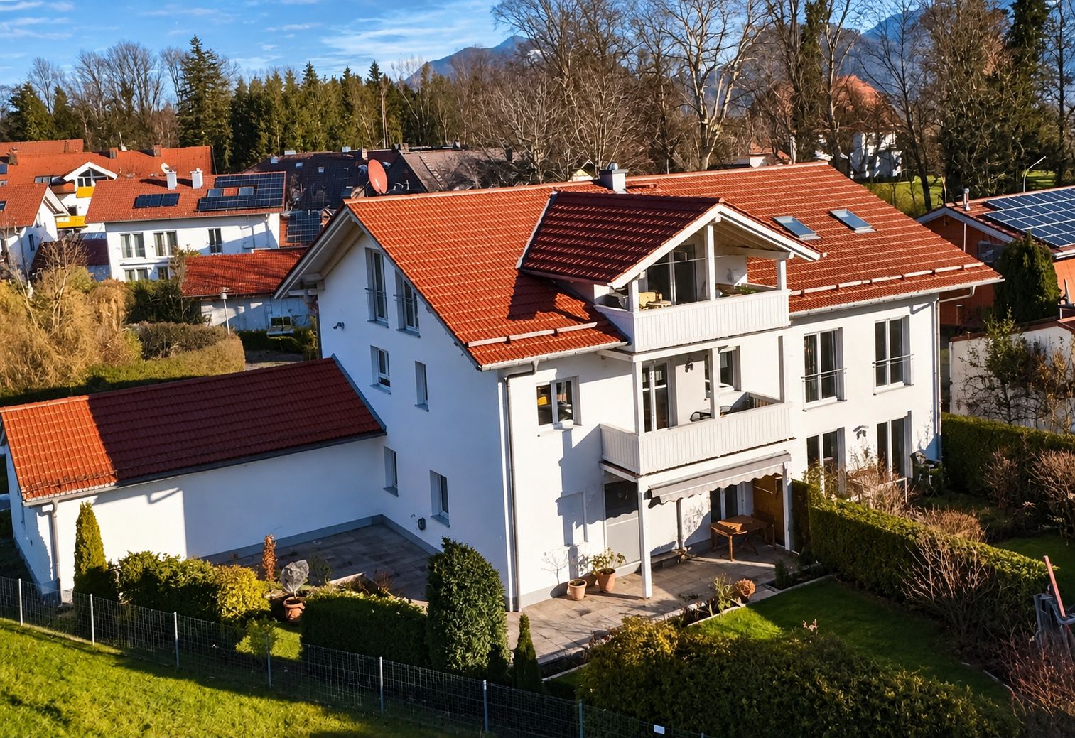 Una casa de dos pisos con techo de tejas rojas, paneles solares y un jardín bien cuidado.