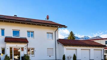Ein zweigeschossiges Gebäude mit rotem Ziegeldach, einer Dreifahrgarage und einem Blick auf die Berge.