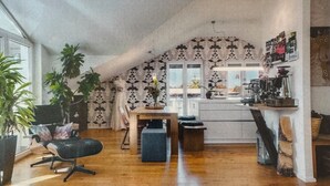 Ein gemütliches Loft-Zimmer mit Holzboden, einem Esstisch, einem schwarzen Stuhl, einer kleinen Sitzecke und einer Küchenzeile mit Arbeitsplatte und verschiedenen Gegenständen.