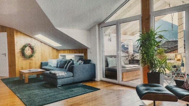 Ein modernes Wohnzimmer mit einem blauen Sofa, einem kleinen Tisch, einem grünen Teppich und einem großen Fenster.