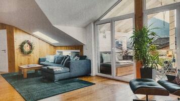 Ein modernes Wohnzimmer mit einem blauen Sofa, einem kleinen Tisch, einem grünen Teppich und einem großen Fenster.