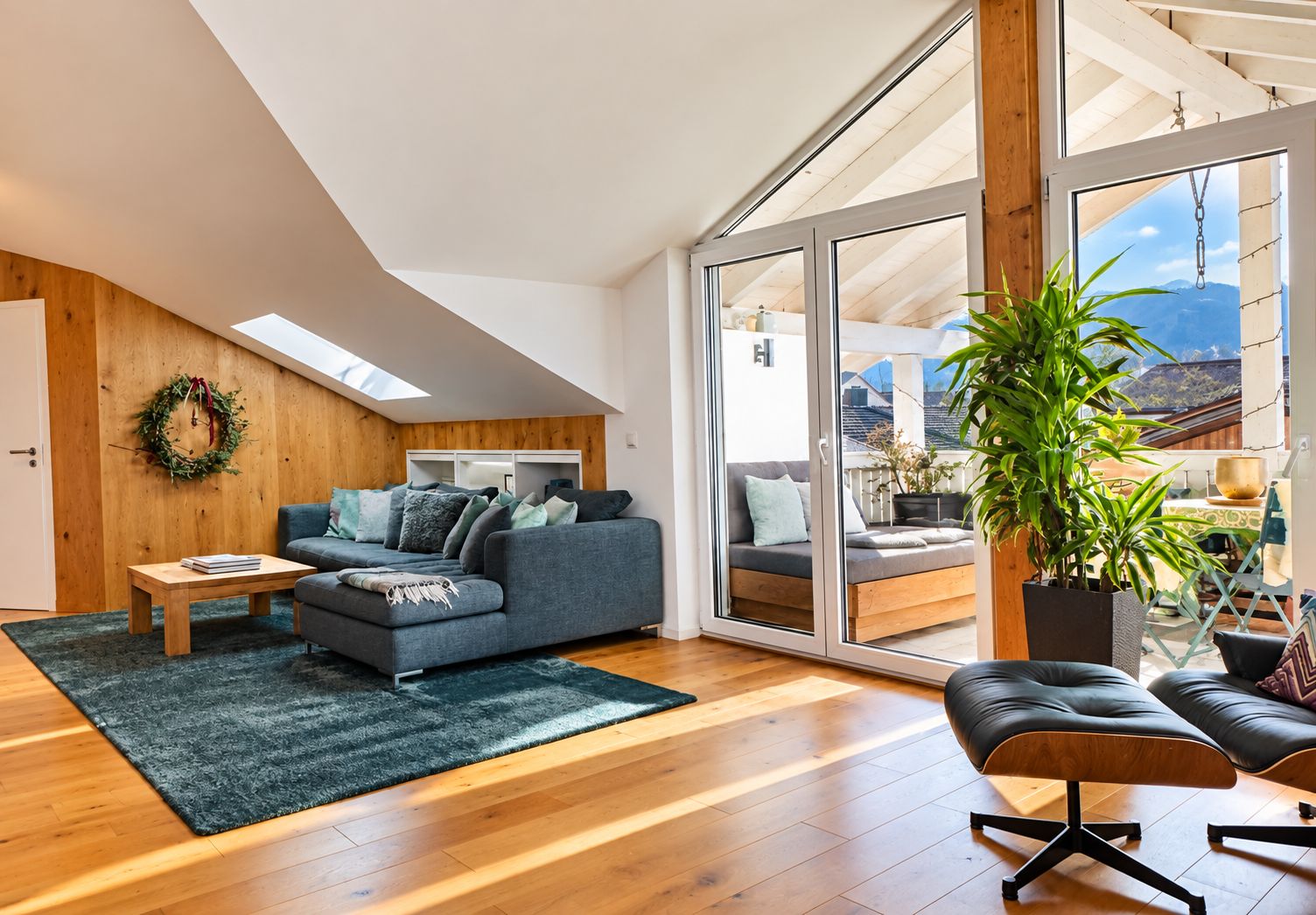 A modern loft apartment with a large sliding glass door leading to a balcony, a grey sofa, a wooden coffee table, and a potted plant.