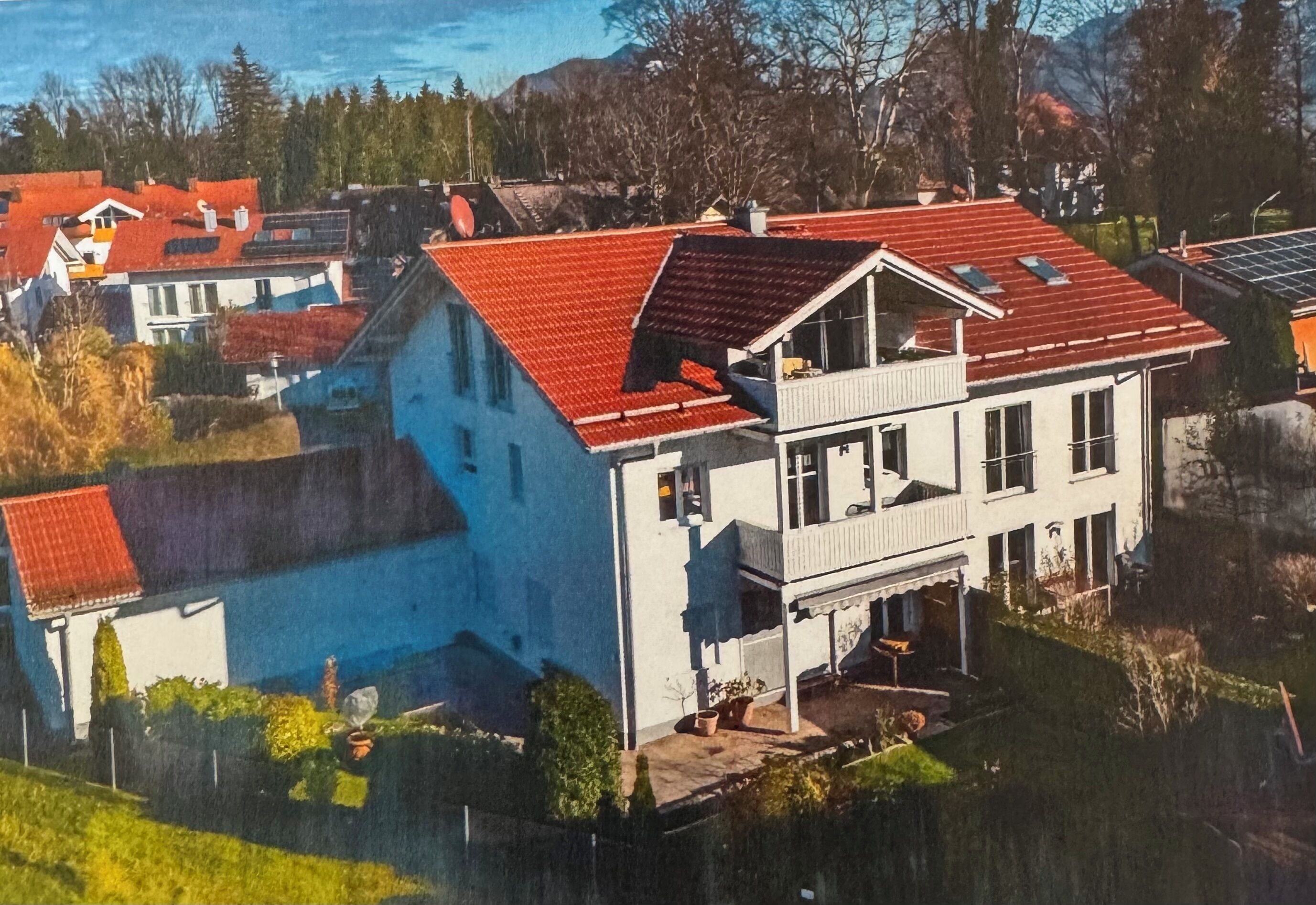 Ein zweistöckiges Haus mit rotem Dach, einem Balkon und einem kleinen Garten.