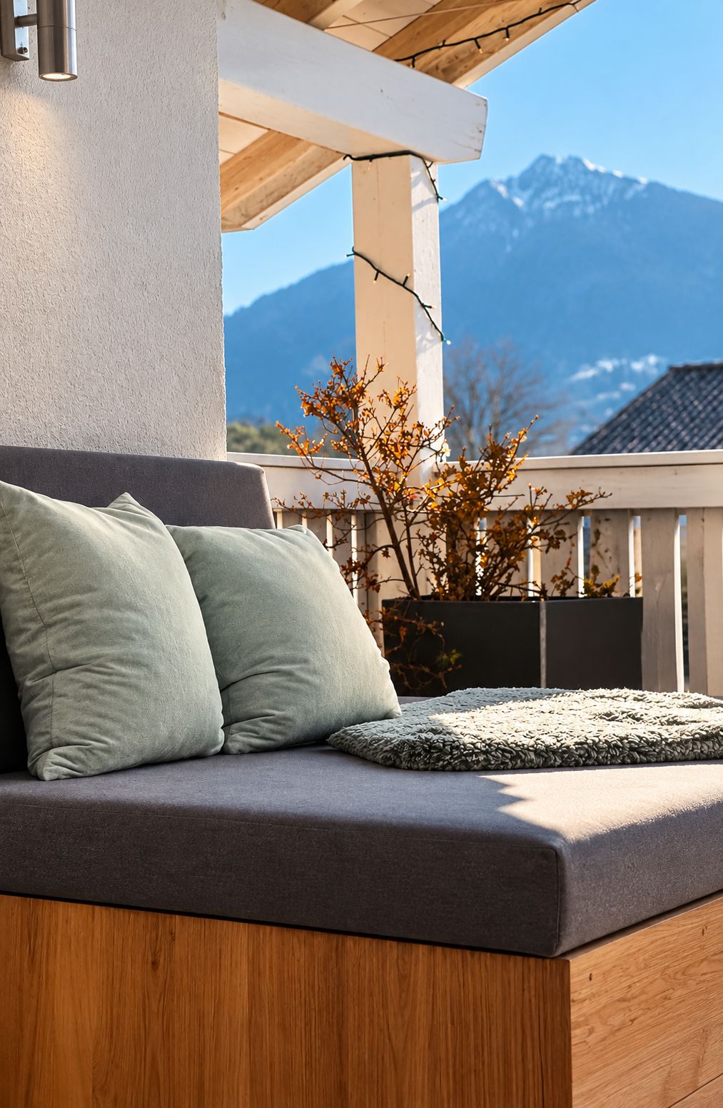 A balcony with a cushioned seating area, a potted plant, and a view of mountains.