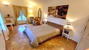 Un dormitorio con una cama grande, un escritorio, una silla, un espejo y un cuadro colgado en la pared.