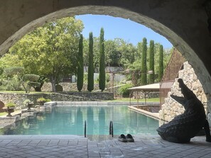 Una piscina al aire libre con un muro de piedra, una terraza de madera y una escultura de piedra.