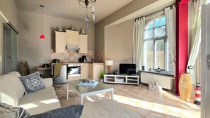 A living room with a sofa, coffee table, and TV, a kitchen with cabinets and appliances, and a large window with curtains. - Vacation apartment S22 - Holiday apartment S22 with terrace and WLAN in Graal-Müritz (Graal-Müritz)