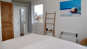 A bedroom with a bed, a wooden ladder, a window, a radiator, and a painting of a boat. - Möwenglück am Meer - Holiday home Möwenglück am Meer with garden by the water (Südbrookmerland)