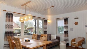 A cozy room with a wooden dining table, chairs, a sofa, and a wicker chair. - Möwenglück am Meer - Holiday home Möwenglück am Meer with garden by the water (Südbrookmerland)