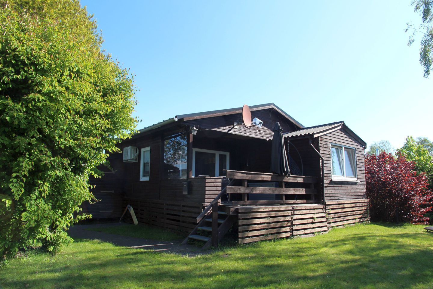 Une cabane en bois dotée d’une véranda, d’une cheminée et d’un petit escalier menant à l’entrée.