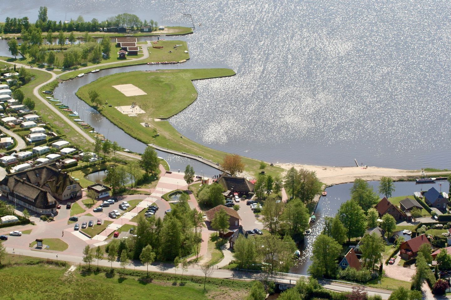 Un quartier résidentiel au bord du lac, avec des maisons, un quai pour bateaux et une plage de sable.