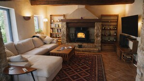 A cozy living room with a stone fireplace, a sofa, a coffee table, a TV, and a bookshelf. - I escape to Umbria, Torreluca (todi)