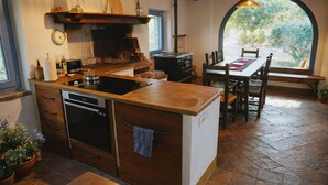 A kitchen with a stove, oven, and sink, a dining table with chairs, and a view through an arched window. - I escape to Umbria, Torreluca (todi)
