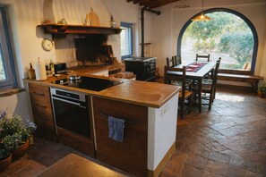 A kitchen with a stove, oven, and sink, a dining table with chairs, and a view through an arched window. - I escape to Umbria, Torreluca (todi)