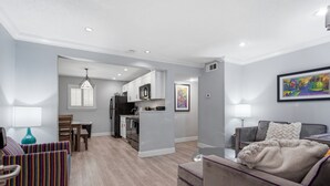 A modern living room with a sofa, a chair, a dining table, and a kitchen area with cabinets and appliances. - Stay steps from the action in this High-end 2BR on Frenchmen Street with pool, hot tub, and easy access to the French Quarter. (New Orleans)