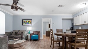 Een woonkamer met een bank, een salontafel, een blauwe fauteuil en een eethoek met een houten tafel en stoelen.