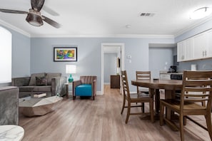 A living room with a sofa, a coffee table, a blue armchair, and a dining area with a wooden table and chairs.